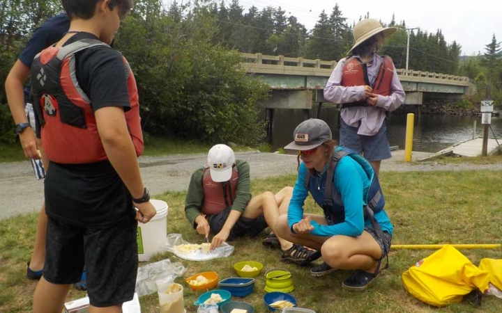 high schoolers eat lunch on canoeing course
